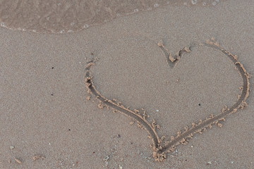 Fototapeta na wymiar drawing heart on the sand near the sea