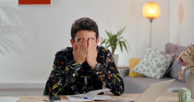 Thoughtful pupil guy studying alone at home school subject to get ready for final exams, nice Hispanic teenager using smart mobile phone calculating math research homework exercise feeling tired