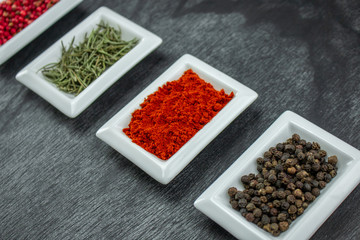 Spices and herbs on wooden table. Pepper, rosemary, tarragon, allspice, turmeric. Colorful spices in white bowls on grey background. Seasonings for cooking. Copy space for text.