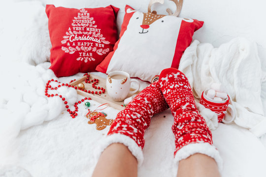 Woman in socks on White Christmas background with cups of cocoa drink and  christmas presents. Cozy winter holidays