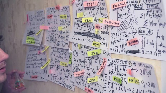 man works with various formulas and calculations on paper sheets that hang on the wall.research work. teacher in the workplace.