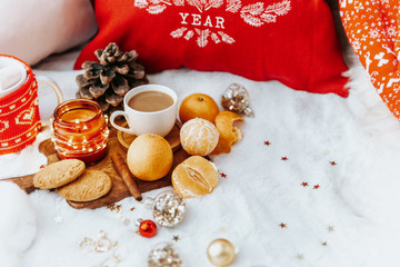 Christmas cozy composition. Winter holiday concept. Cup with coffee, tangerines, cookies, and decorations on the bed