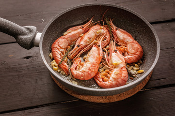 Close-up King shrimps fried in a ceramic pan on a dark wooden table