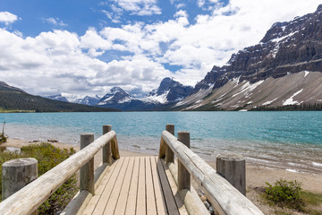 wooden pier by a beautiful aqua coloured lake with mountains and blue sky in the background in the summer time