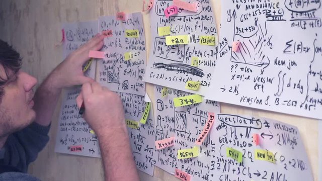 researcher works with various formulas and calculations on paper sheets that hang on the wall.research work.scientist in the workplace