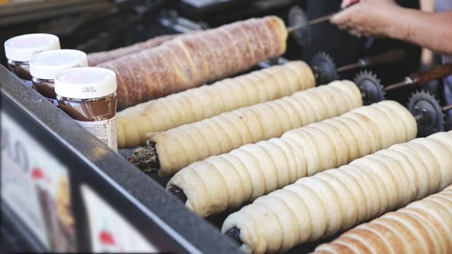 Traditional baking of old Bohemian pastry trdelnik - sweet spit pastry from rolled dough wrapped around stick and grilled