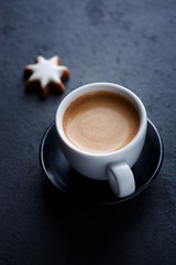 Cup of coffee and Christmas cookie (cinnamon stars) on dark stone background. Close up. 