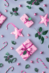 Toned two tone duochrome Christmas background with pink gift boxes, stripy candy canes, trinkets and decorative stars. Geometric creative flat lay on silver paper in pink, magenta and green.