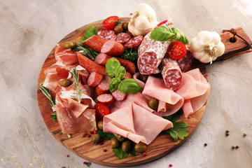 Food tray with delicious salami, pieces of sliced prosciutto crudo, sausage and basil. Meat platter