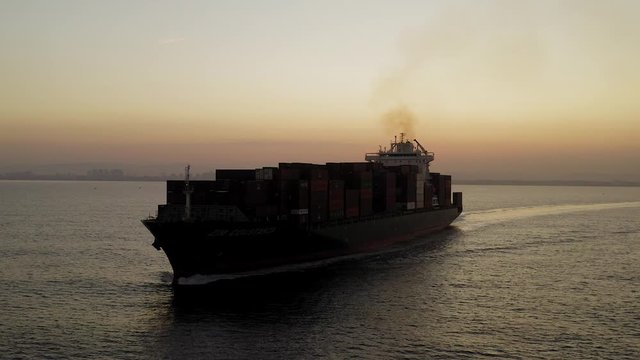 Large Container ship cruising slowly  across the open sea at Sunrise, Aerial follow footage.