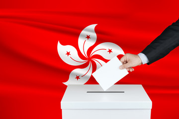 Election in Hong Kong. The hand of man putting his vote in the ballot box. Waved Hong Kong flag on background.