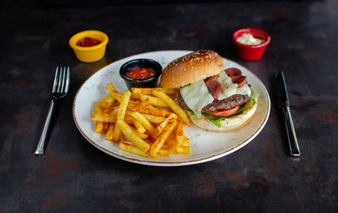 Beef burger, french fries and ketchup on rustic metallic background.