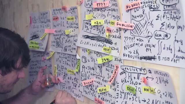 man works with various formulas and calculations on paper sheets that hang on the wall.research work. teacher in the workplace