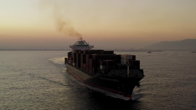 Large Container ship cruising slowly  across the open sea at Sunrise, Aerial follow footage.