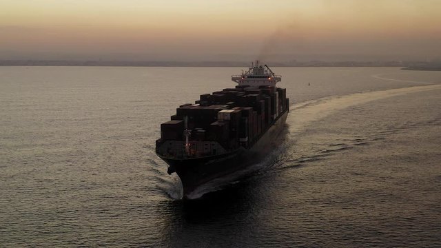 Large Container ship cruising slowly  across the open sea at Sunrise, Aerial follow footage.