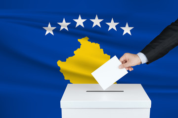 Election in Kosovo. The hand of man putting his vote in the ballot box. Waved Kosovo flag on background.