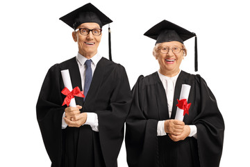Elderly people in graduation gowns holding diplomas