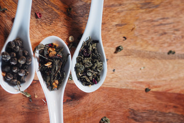 Different varieties of tea leaves in white measuring spoons on a wooden table. To brew tea