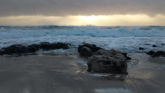 Waves gently washing and crashing across large rocks on a beach during sunrise