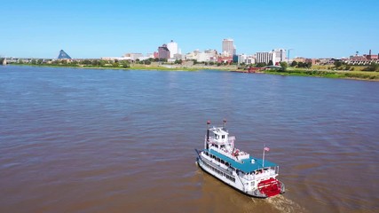 Good aerial of a paddlewheel steamboat riverboat moving up the Mississippi River with Memphis Tennessee in the background.