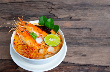 Tom Yum Goong or Shrimp soup spicy sour Soup Traditional food in Thailand contains chili, lime,lemongrass, lime leaf, along with cooked rice in a white dish on the old wood background.