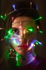 Naklejka premium Portrait of a girl with the lights on her face. New Year portrait. Unhappy girl. Holiday.