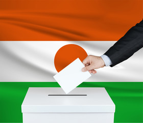 Election in Niger. The hand of man putting his vote in the ballot box. Waved Niger flag on background.