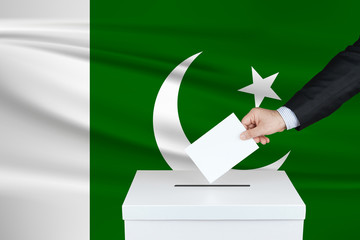 Election in Pakistan. The hand of man putting his vote in the ballot box. Waved Pakistan flag on background.
