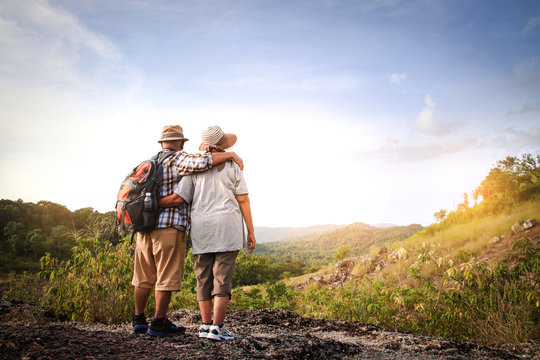 The elderly couple, hiking and standing on a high mountain, are happy in retirement.