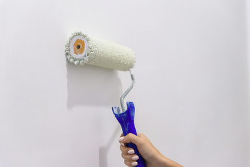 Painting out a white wall with a paint roller with white paint. Close up female hand painting wall...