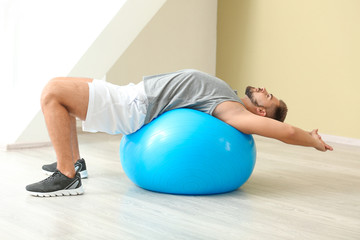 Sporty young man training with fitball in gym