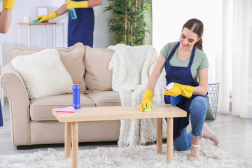 Female janitor cleaning table in room