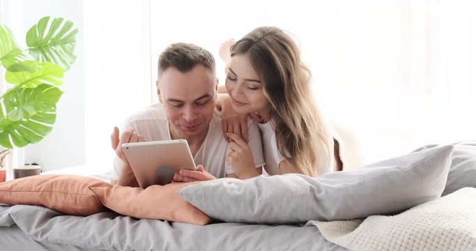 Young couple having fun while reading on digital tablet in bed at home