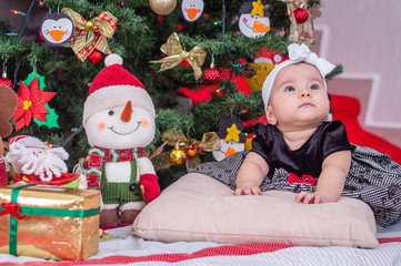 Obraz na płótnie Canvas A white baby, Christmas tree decoration with black dress and white bow, on the cushion, looks impressed above