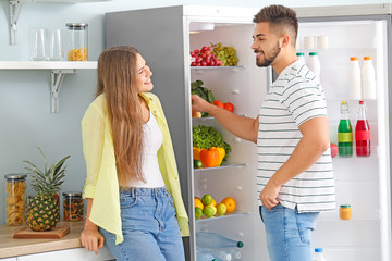Young couple taking food out of fridge in kitchen