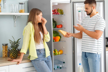 Young couple feeling bad smell from fridge in kitchen - obrazy, fototapety, plakaty