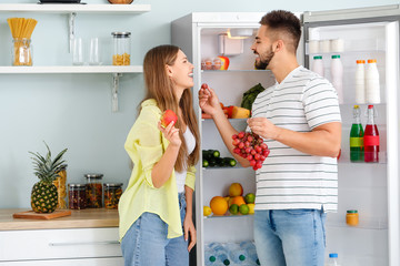 Young couple taking food out of fridge in kitchen