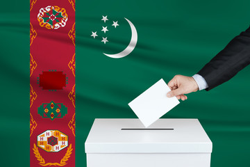Election in Turkmenistan. The hand of man putting his vote in the ballot box. Waved Turkmenistan flag on background.
