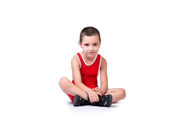 Sporty cheerful boy in a blue wrestling tights is ready to engage in sports exercises, is sitting on the floor on a white isolated background