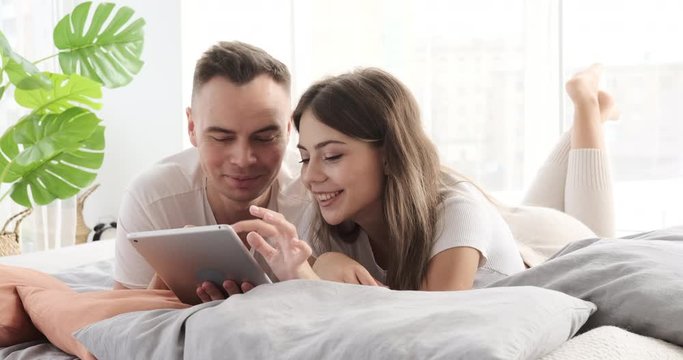 Couple having fun using digital tablet lying on bed at home