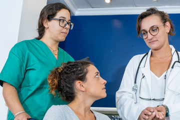 Doctor holding the hand of a girl in a wheelchair accompanied by a nurse