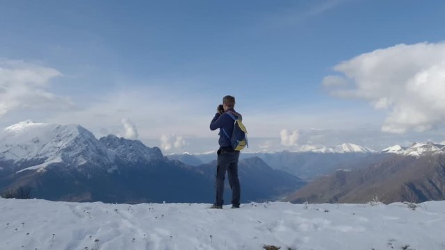 Man photographs the snowy mountains form a lookout. 4k
