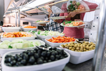 Plates with chopped pepper, tomatoes, olives and salad at a self-service restaurant counter