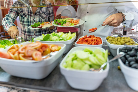 Detail of people's hands taking food from a self-service restaurant full of healthy food