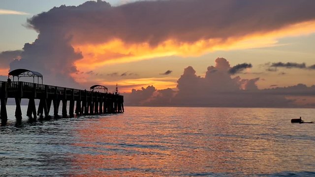 A wooden pier stretching out into the ocean is framed by a background of color during a beautiful sunrise over the ocean