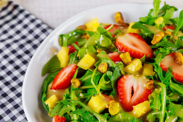 Salad with arugula, strawberries, mango and pistachios.