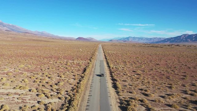 Aerial of a 4WD wheel drive vehicle on a paved road across the Owens Valley desert region suggests remote Eastern Sierra adventure.