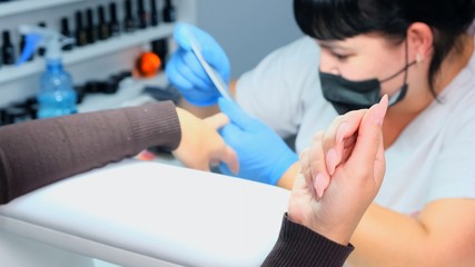 Manicurist files a nail with a nail file to a client. Manicure process, nail extension. close-up