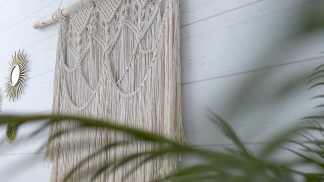 white macrame hanging on a wall through green leaves