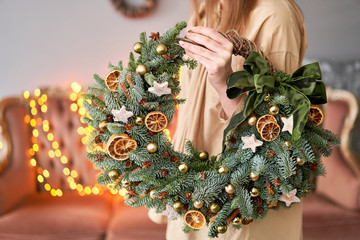 Christmas mood. Beautiful festive wreath of fresh spruce in woman hands. Xmas tree. Bokeh of...